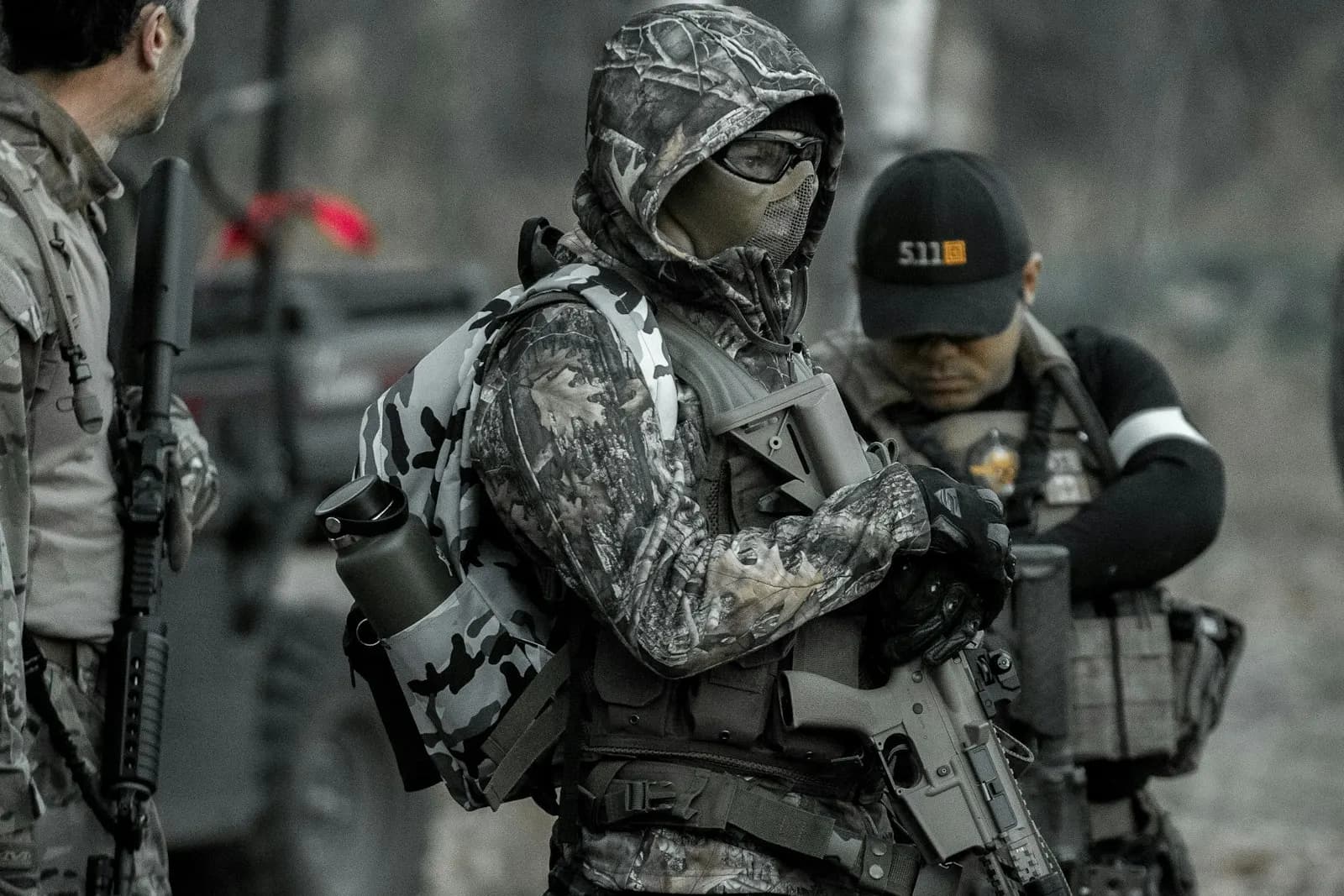 Groupe de joueurs d'airsoft équipés en tenue camouflage, avec casquettes et répliques, réunis en extérieur
