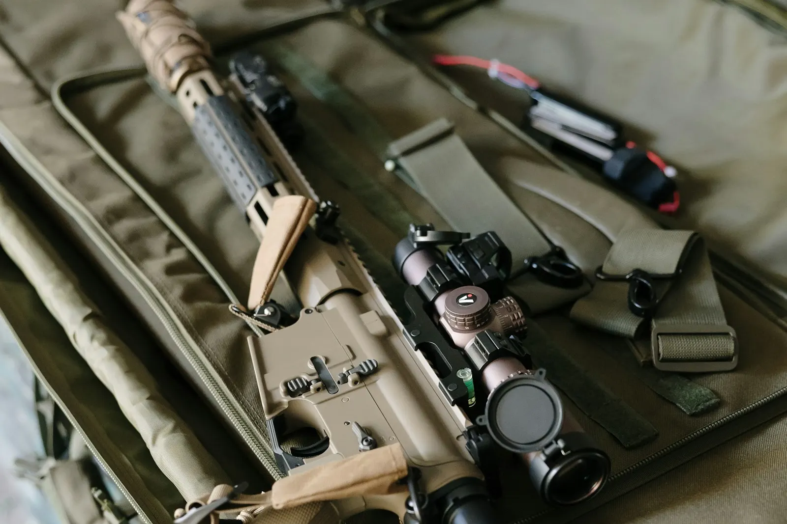 Réplique d'airsoft couleur sable équipée d'une lunette, rangée dans une housse de transport matelassée