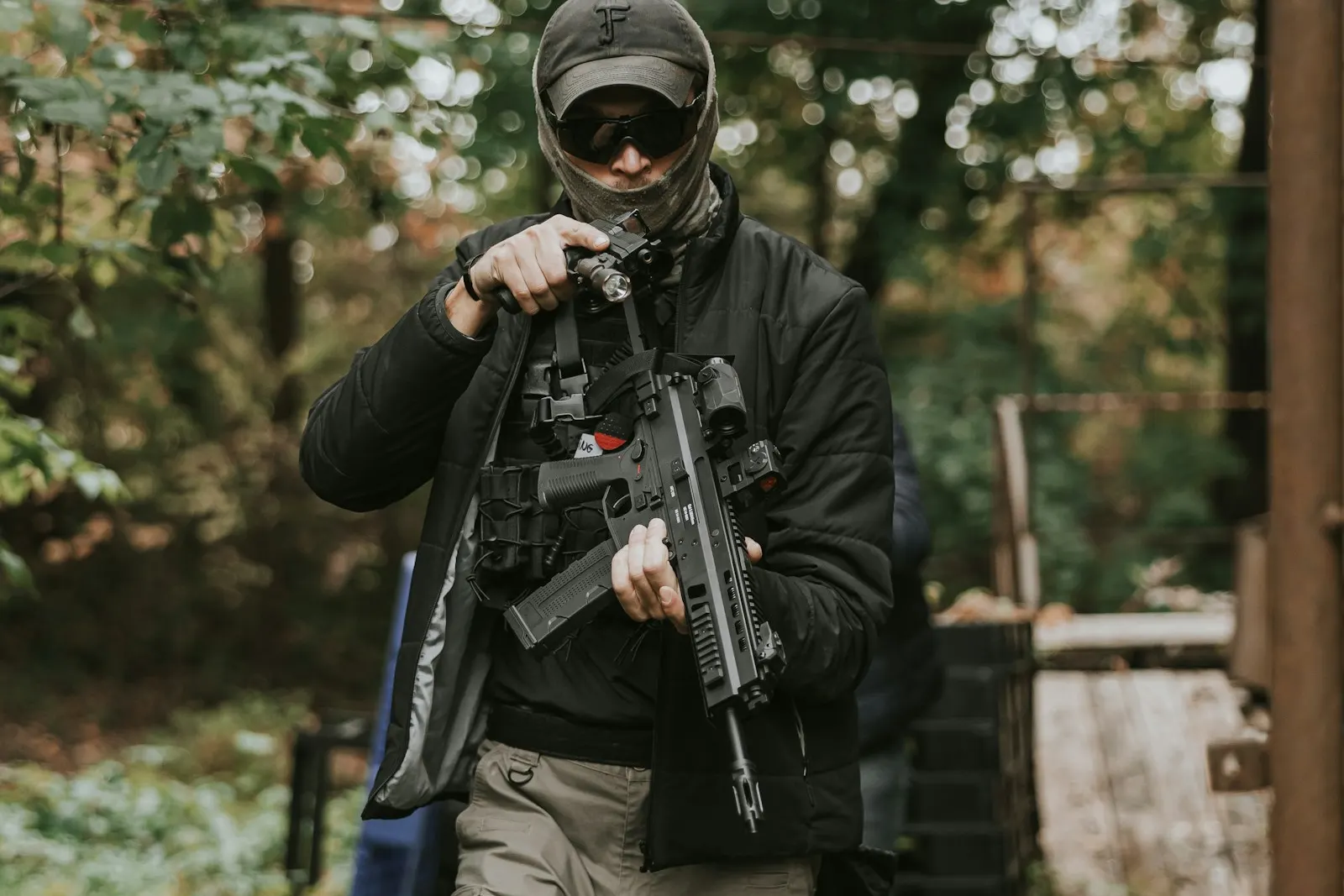 Joueur d'airsoft portant casquette et lunettes de protection, manipulant sa réplique en lisière de forêt