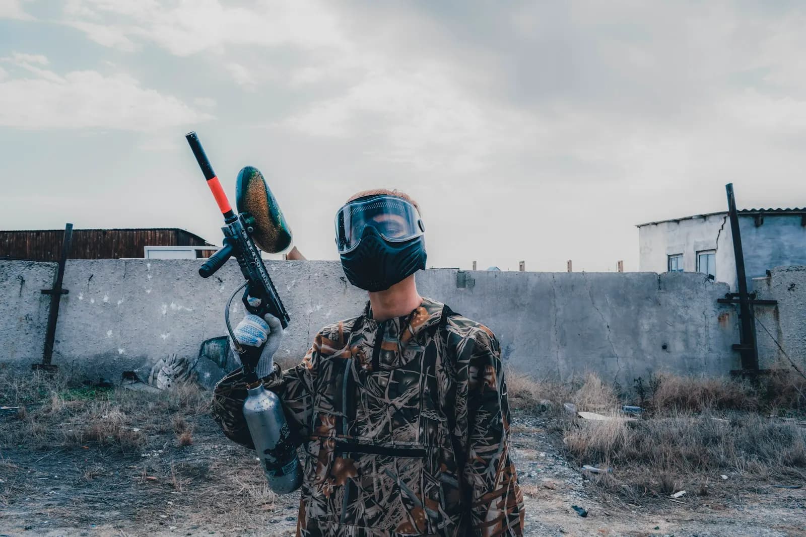 Joueur de paintball en tenue camouflage tenant son lanceur équipé d'une trémie, masque sur le visage