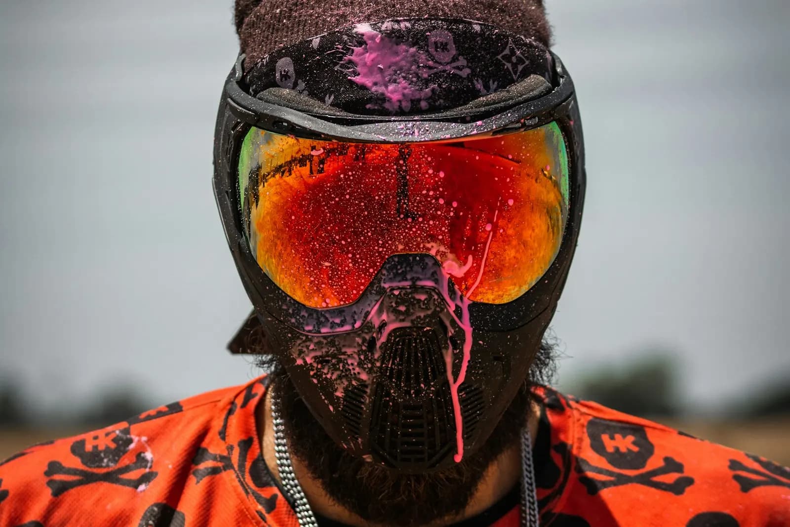 Joueur de paintball portant un masque intégral à écran orange couvert de traces de peinture rose