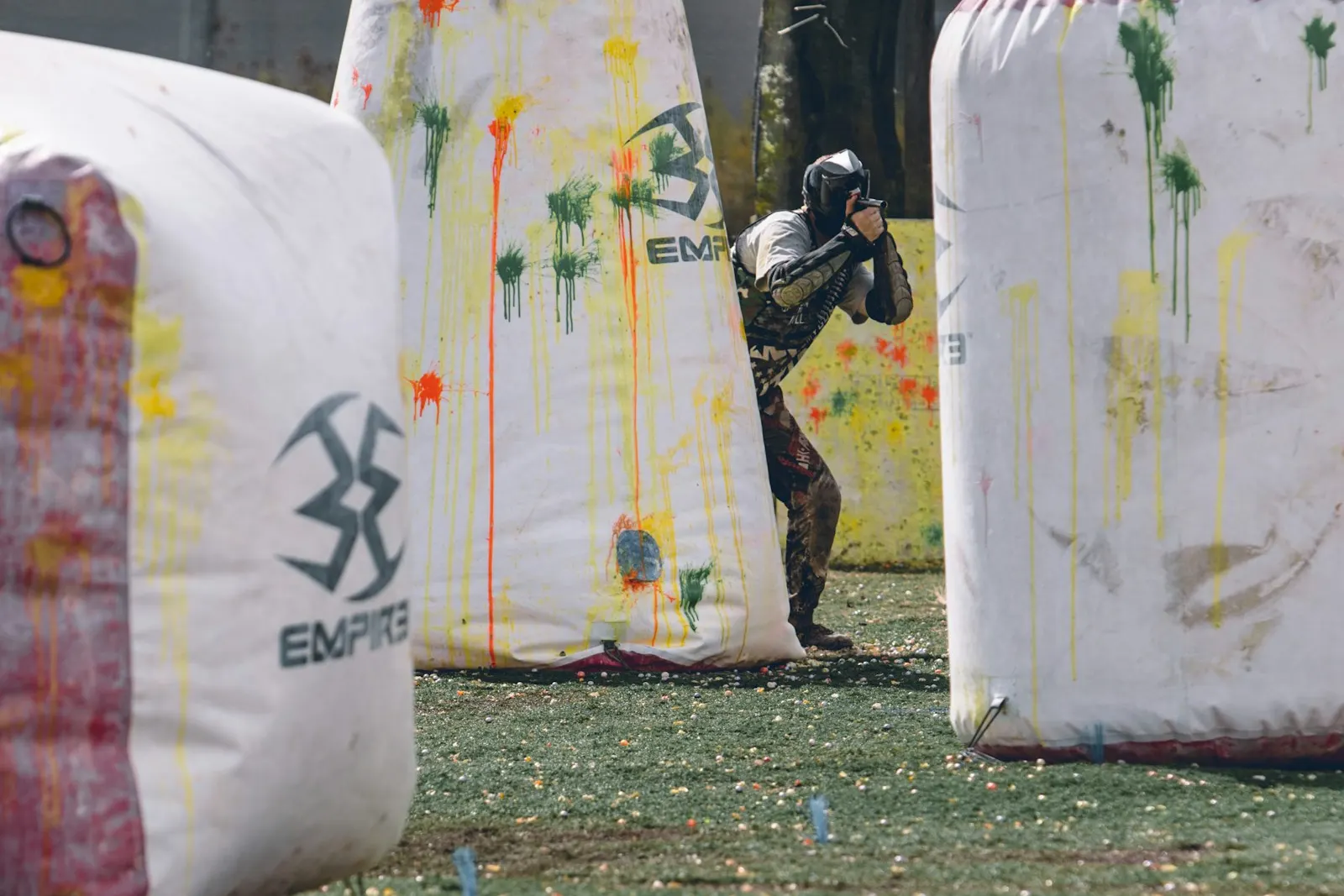 Joueur de paintball à l'abri derrière des obstacles gonflables tachés de peinture sur un terrain de speedball