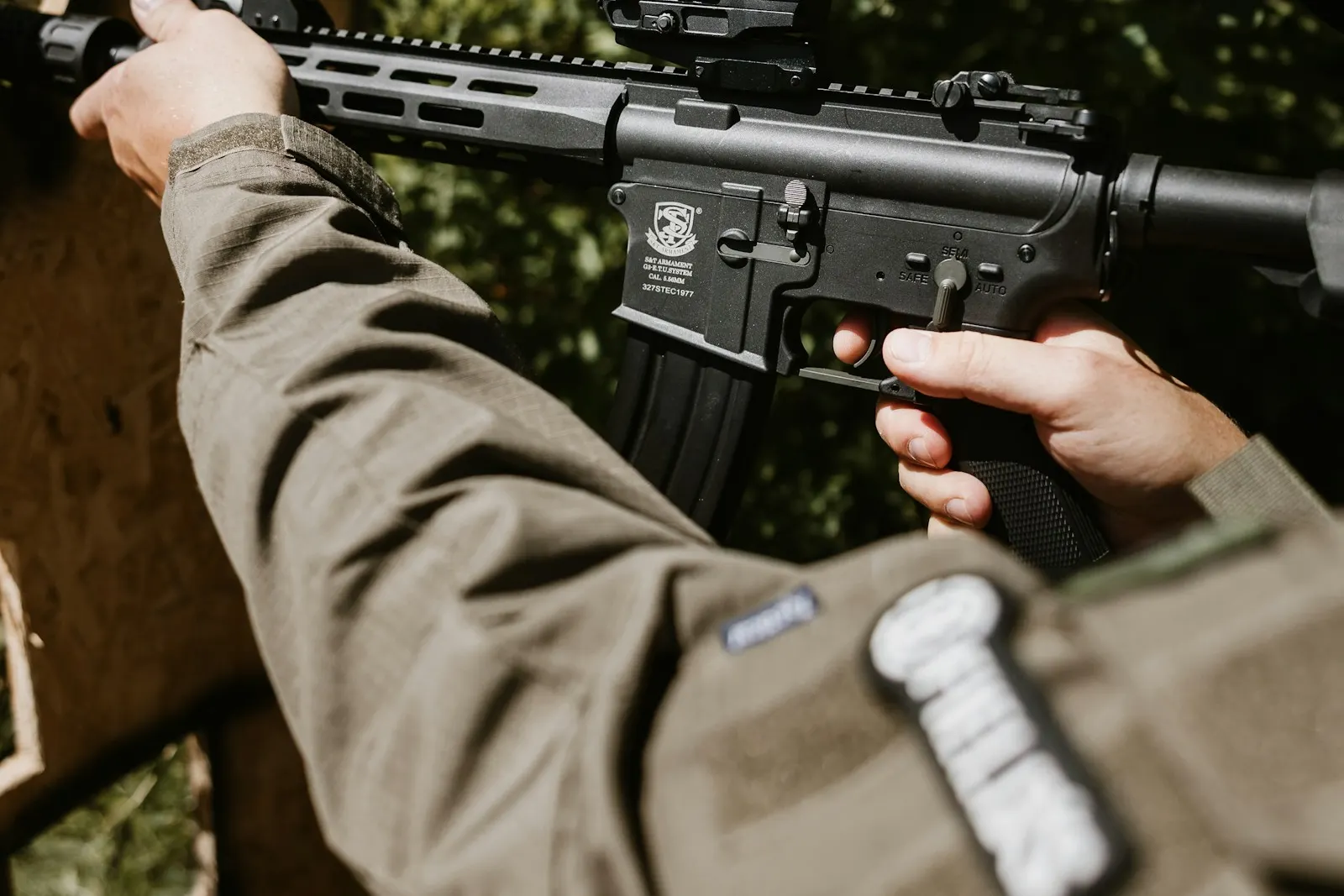 Gros plan sur le bras d'un joueur d'airsoft portant un écusson sur la manche, tenant une réplique noire