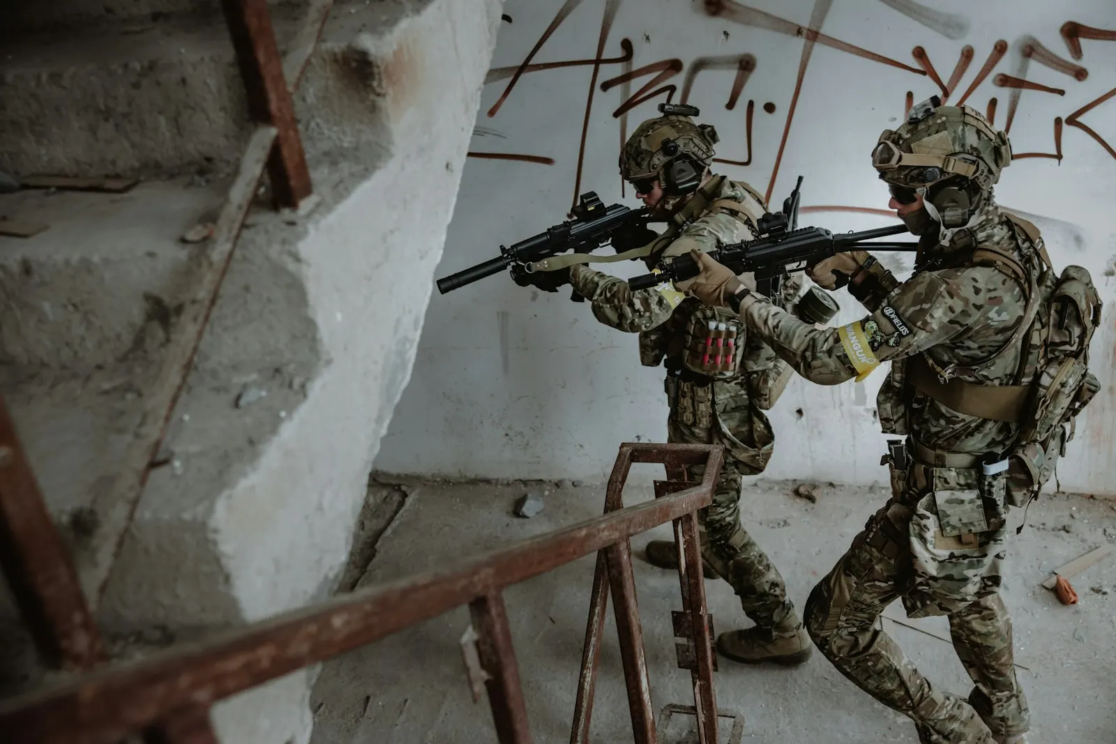 Deux joueurs d'airsoft en tenue camouflage progressant en binôme dans un bâtiment aménagé aux murs tagués