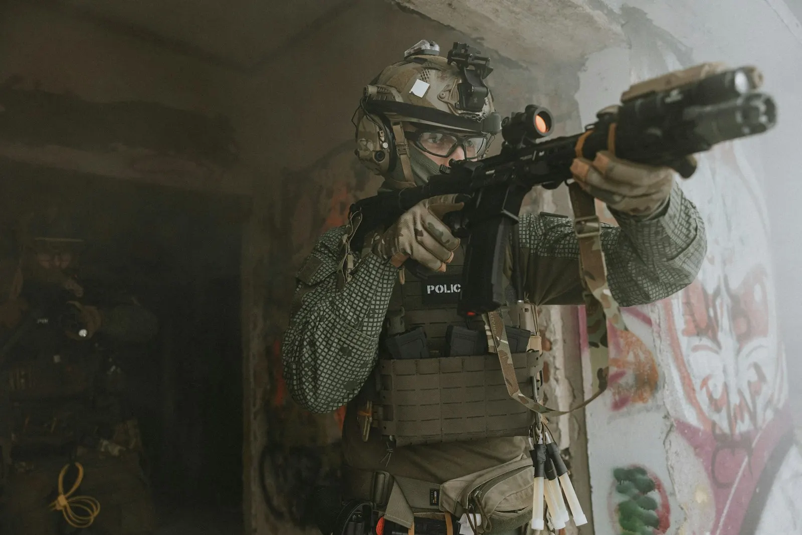 Joueur d'airsoft équipé d'un casque et d'un gilet, réplique épaulée, franchissant une porte dans un bâtiment enfumé