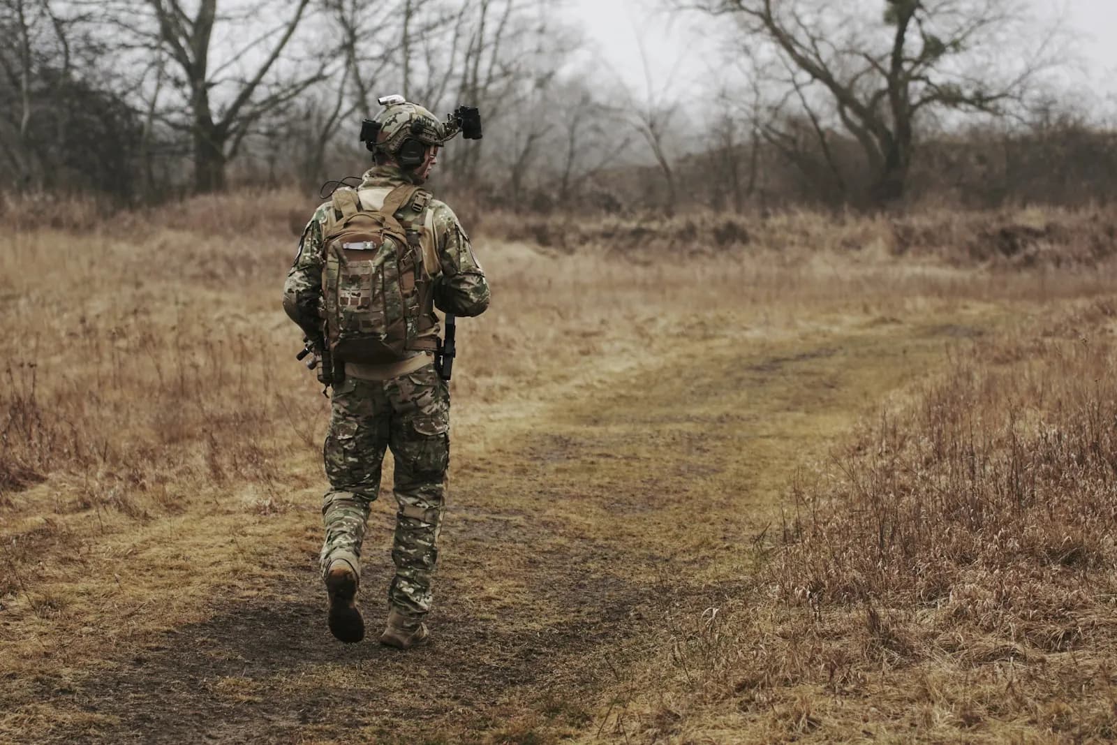 Joueur d'airsoft en tenue camouflage marchant sur un chemin de terre dans un terrain extérieur boisé