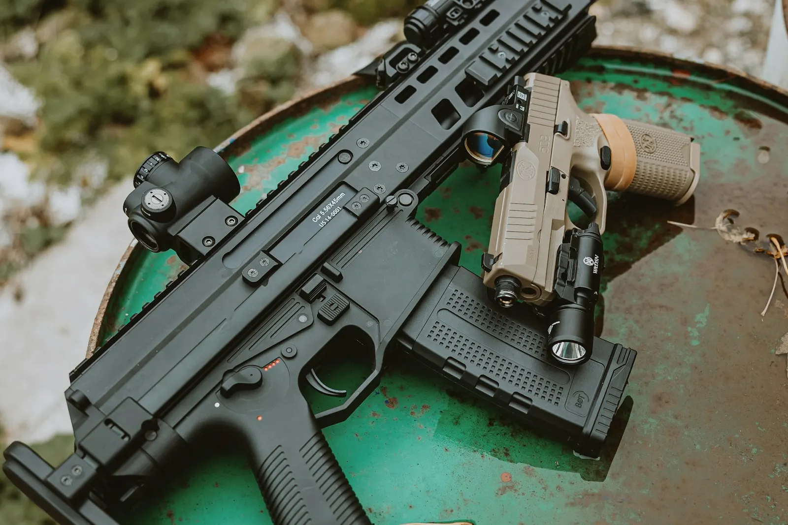 Réplique d'airsoft compacte équipée d'un point rouge et pistolet couleur sable posés sur un fût métallique vert