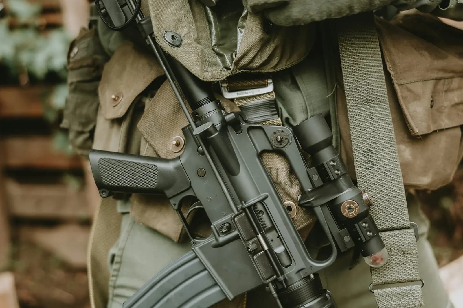 Réplique d'airsoft noire équipée d'une lunette et d'une lampe, portée en bandoulière par un joueur en veste militaire