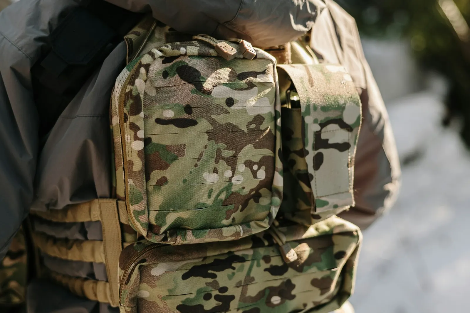 Joueur d'airsoft portant un sac à dos camouflage multicam sur un gilet tactique, en extérieur