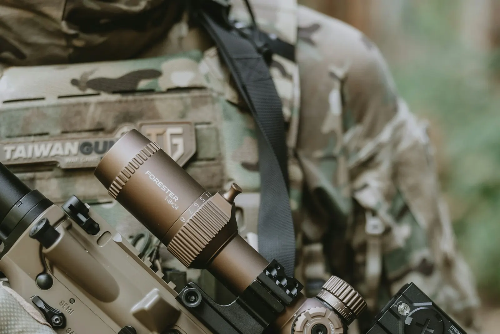 Réplique d'airsoft de type DMR couleur sable équipée d'une lunette de visée, portée par un joueur en tenue camouflage