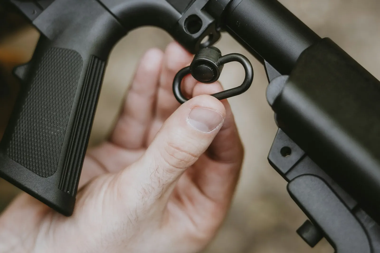 Gros plan sur des mains fixant une attache de sangle à l'arrière d'une réplique d'airsoft noire