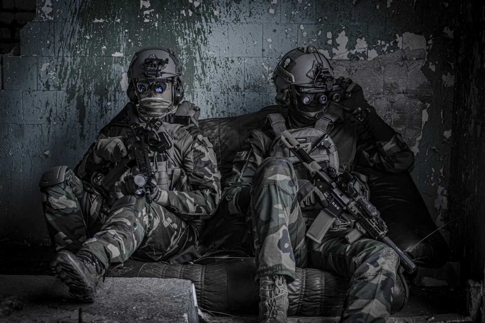 Deux joueurs d'airsoft équipés de casques et de dispositifs de vision nocturne, assis dans un bâtiment sombre