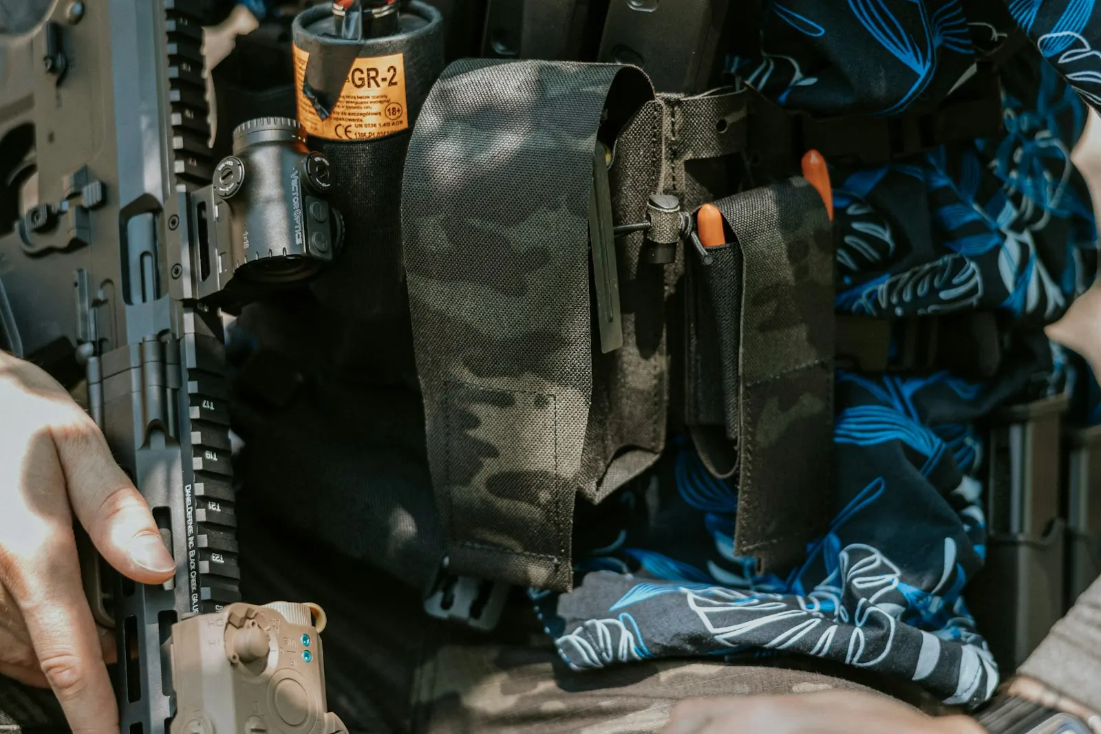 Joueur d'airsoft portant un équipement léger avec poches et pochette sur une chemise à motifs bleus, réplique en main